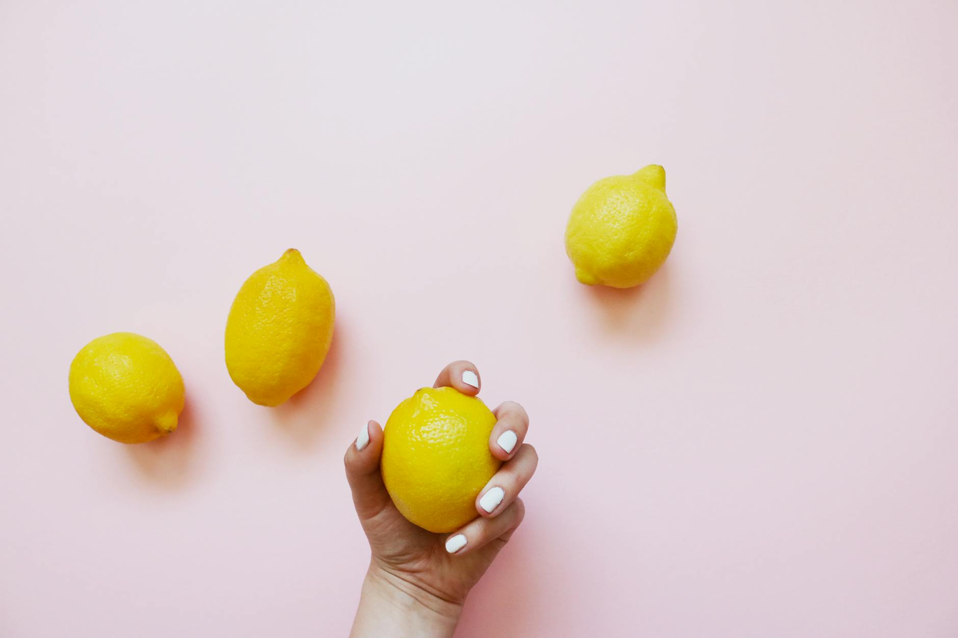 A hand holding a fresh lemon on a soft pink background, surrounded by additional lemons, symbolizing the gentle, natural approach of lemon vibrators