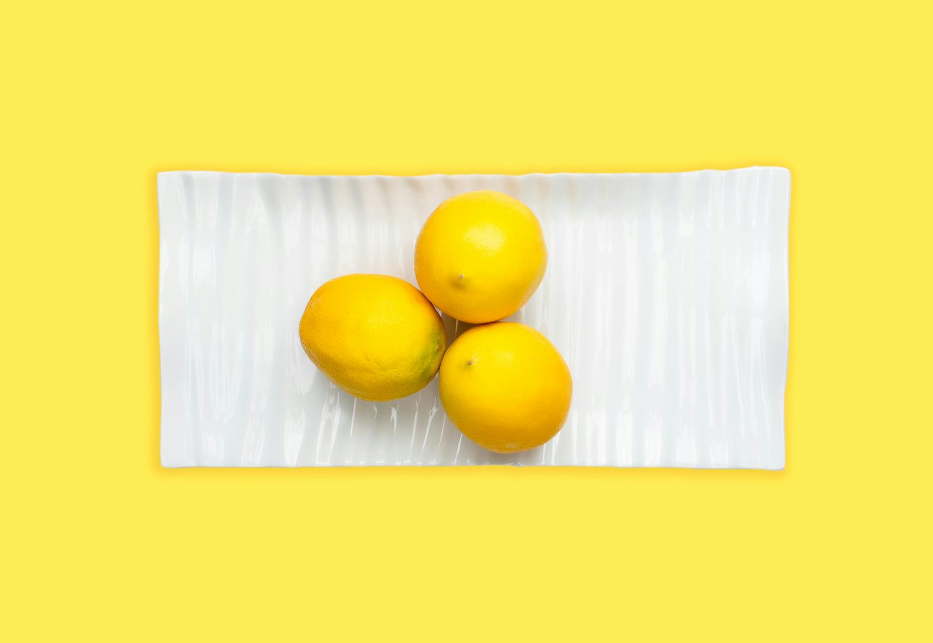 Trois citrons frais arrangés sur une assiette blanche avec un arrière-plan jaune vibrant, symbolisant la fraîcheur et l'énergie du plaisir