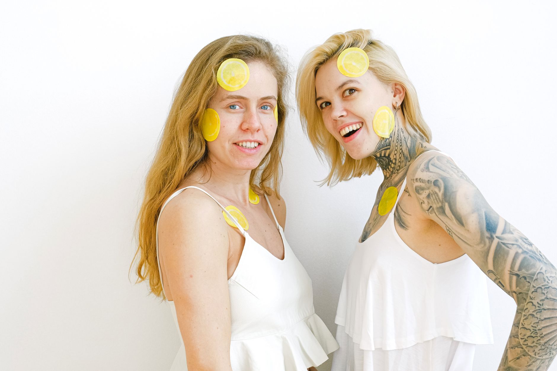 Two women laughing together with lemon slices on their faces, symbolizing joy and intimate connection