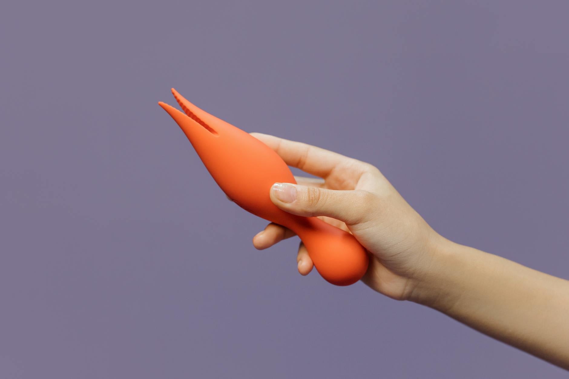 Hand mit orange Vibrator gegen minimalistischen lila Hintergrund
